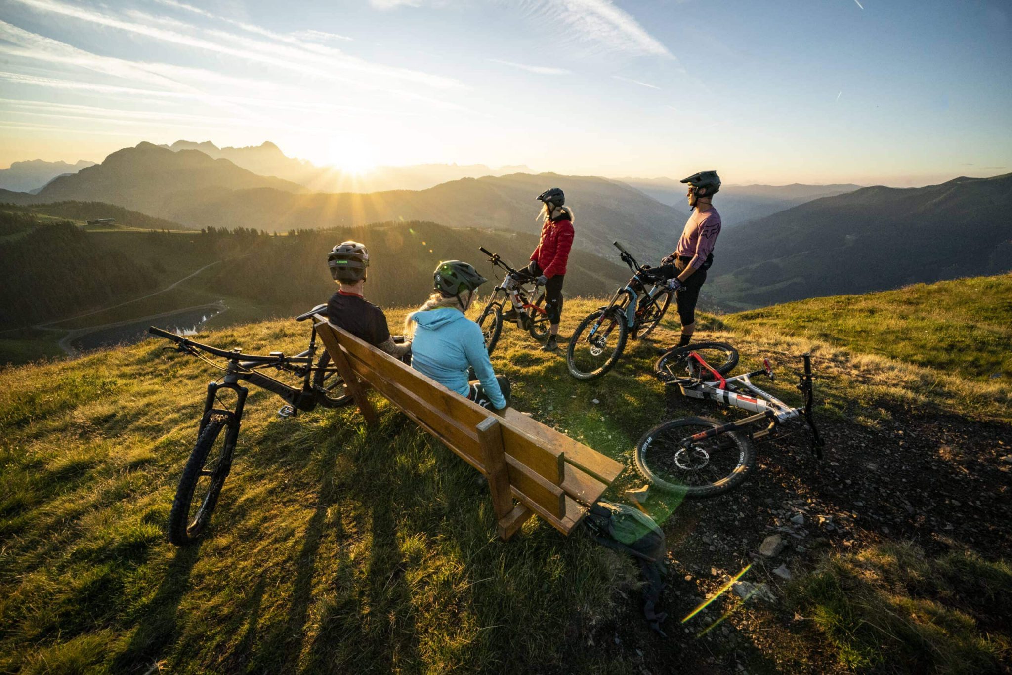 Mountainbiker genießen den Sonnenuntergang über den Pinzgauer Grasbergen in Saalbach Hinterglemm.