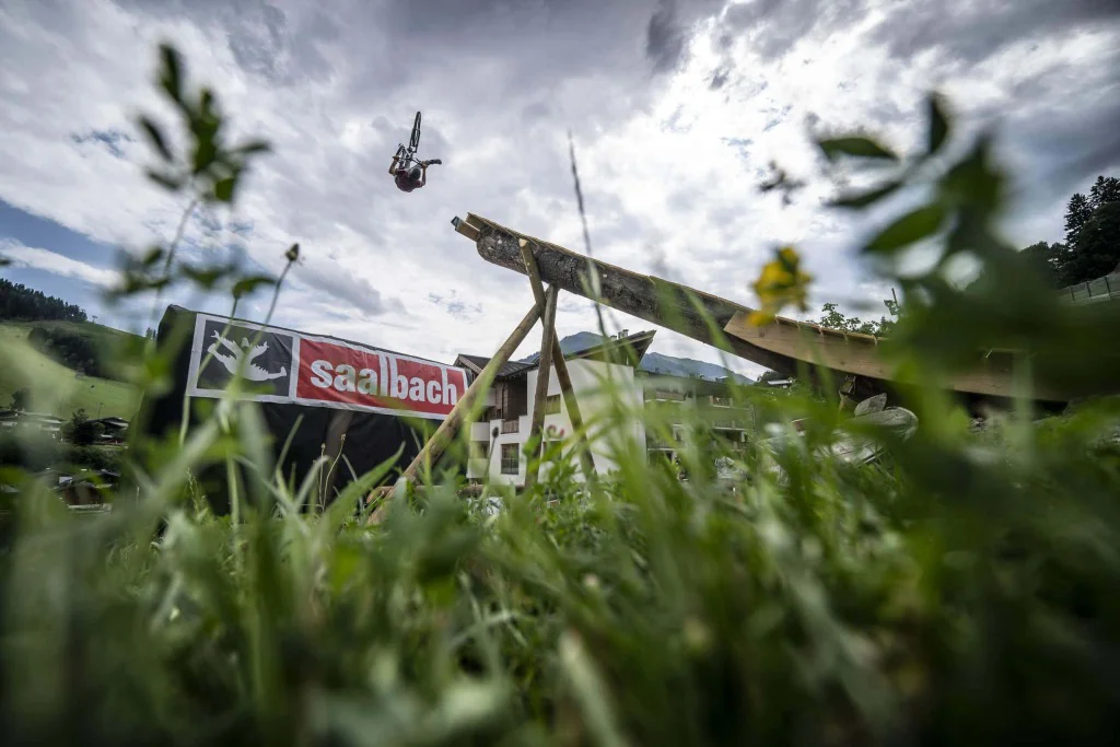 Mountainbiker zeigt Stunt in Saalbach, umgeben von beeindruckender alpiner Umgebung