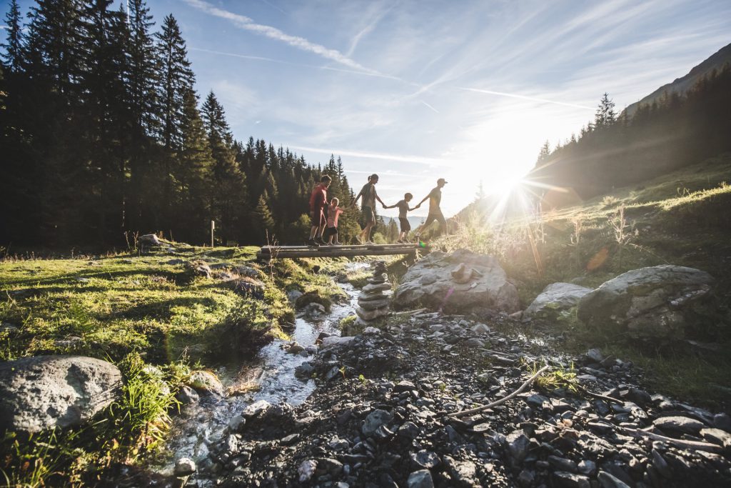 Familie beim Wandern im Pinzgau, im Vordergrund ein glitzernder Gebirgsbach und Sonne.