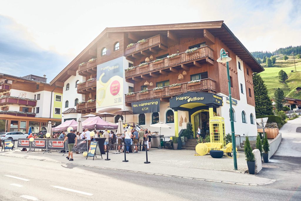 Hotelansicht mit Gästen im Freien, umgeben von Bergen in Saalbach Hinterglemm.